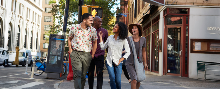 Four friends laugh together while walking in a sunny American city