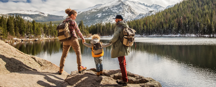 A family with a young child stands on a boulder overlooking an alpine lake in a US national park.